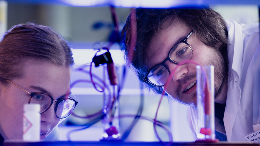 To studenter arbeider med reagensrør og ledninger i et laboratorium.