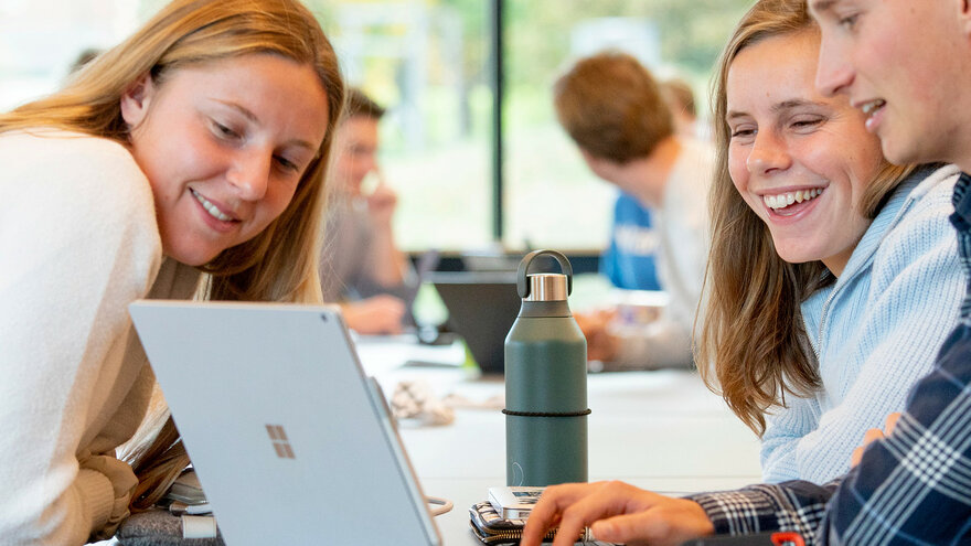 To kvinnelige og en mannlig student ser på en laptop sammen