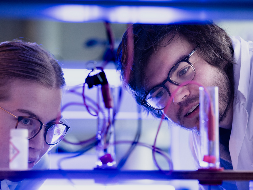 To studenter arbeider med reagensrør og ledninger i et laboratorium.