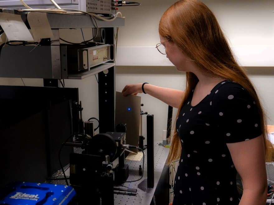 Ung kvinne med briller står foran måleutstyr for lys i et laboratorium.