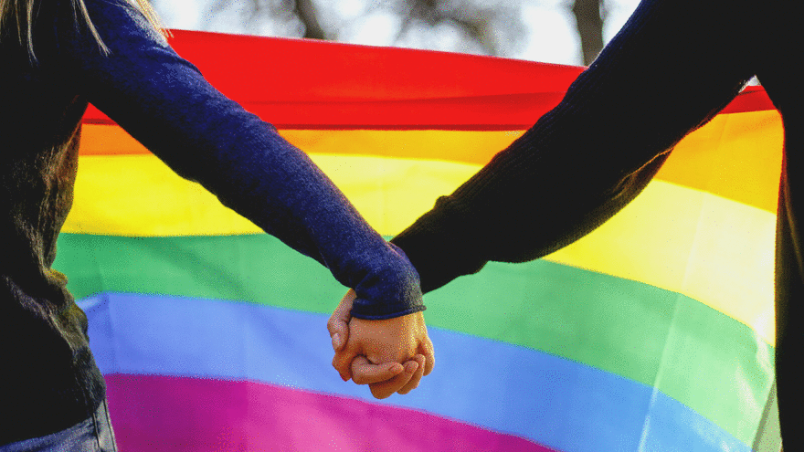To mennesker holder hender med Pride-flagget i bakgrunnen