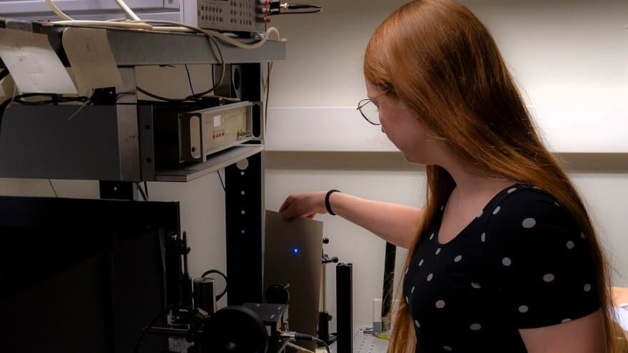 Ung kvinne med briller står foran måleutstyr for lys i et laboratorium.